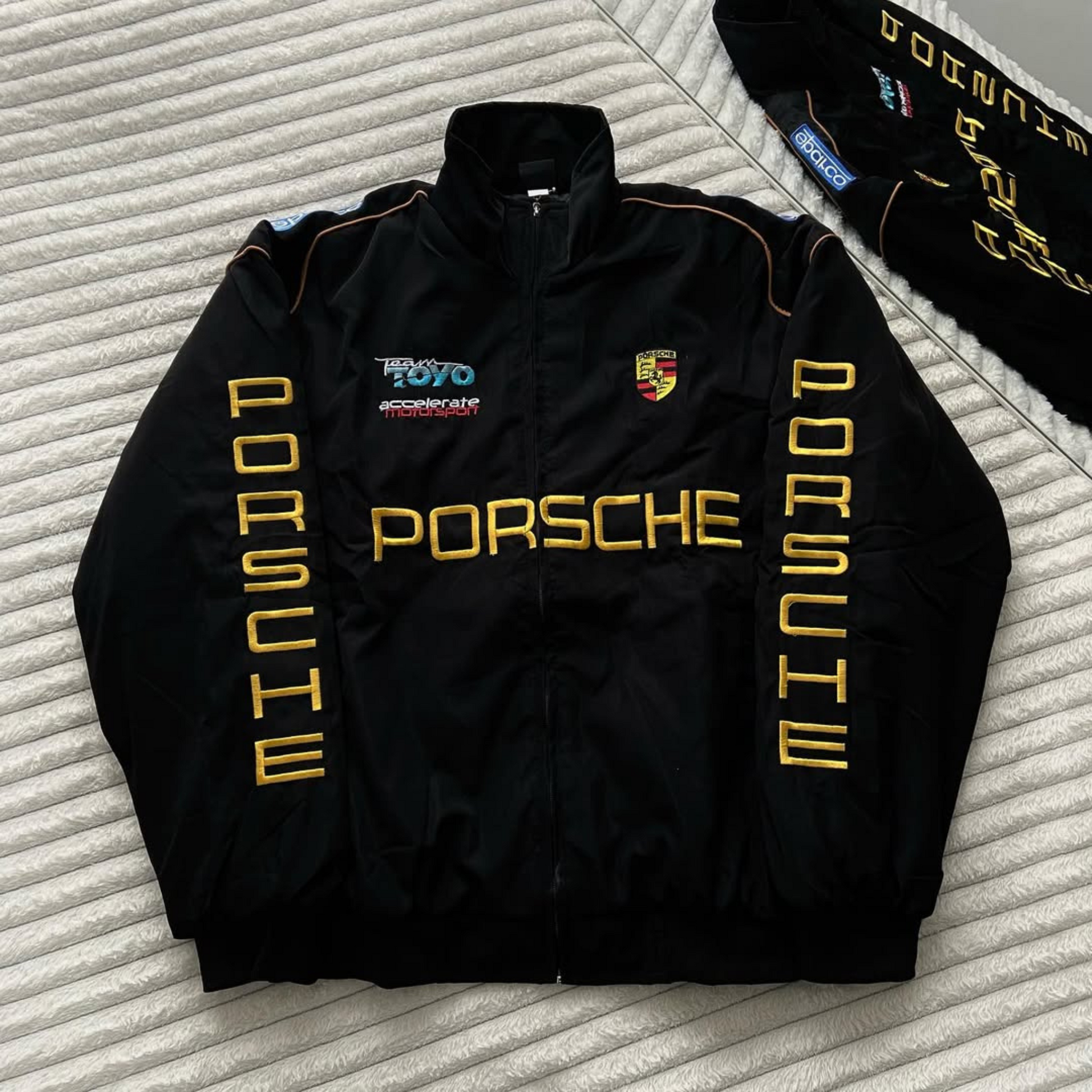 Black Porsche puffer jacket with premium embroidered logo and quilted padding for luxury motorsport streetwear.